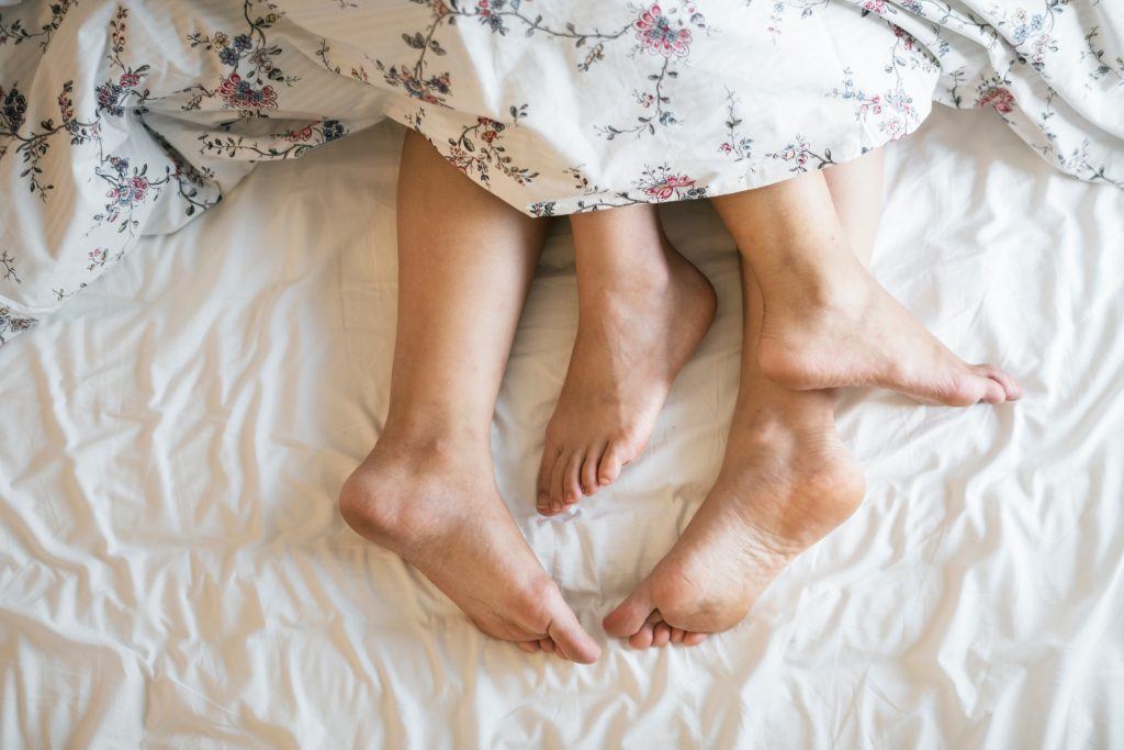 Adults Barefoot In Bed, Covered With Sheets