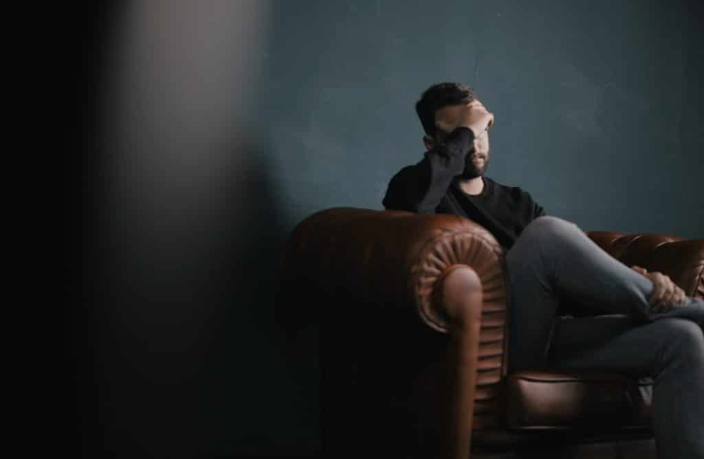 A Man Holds His Head While Sitting On A Sofa